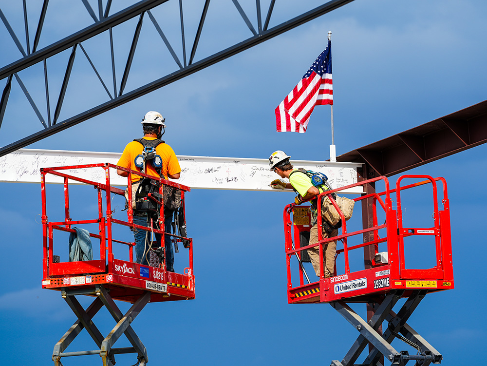 Workers signing steel beam on boom lifts