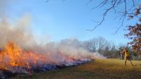 Man points fire hose at burning prairie grass fire