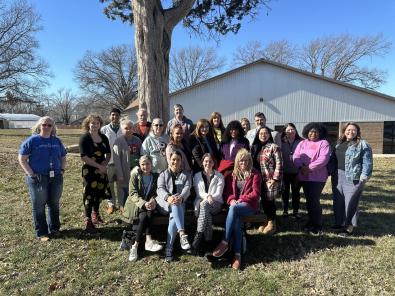 Photo of individuals involved in the Housing Stabilization Collaborative. Photo is outside, in front of a building and a tree with everyone standing except for four individuals sitting on a bench. Everyone is smiling. 