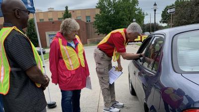 Individuals wearing hi rez vests gather outside of a vehicle
