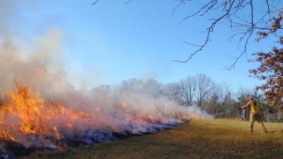 Man points fire hose at burning prairie grass fire