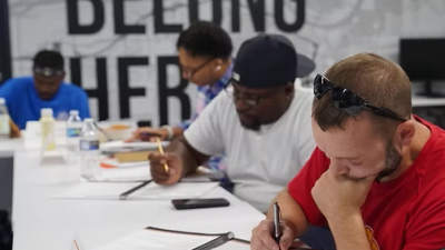 People at long tables looking down while filling out a notebook
