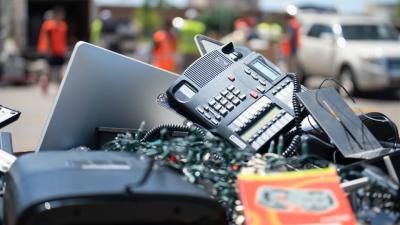 Pile of old electronics heaped and in focus with background blurred of people in hi-res vests and vehicles