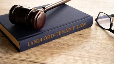 A gavel rests on top of a book labeled landlord tennant law both on top of a table with a pair of glasses